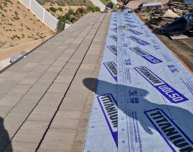 A sloped roof under renovation, showcasing a layer of blue Titanium UDL50 underlayment and nearby stacked roofing materials.
